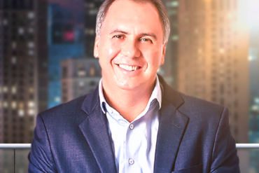 Marcos Trombetti em pose de inspiração com símbolos de riqueza ao redor, promovendo o download de Ideias Milionárias.