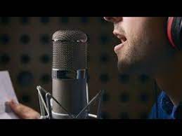 Homem sorrindo e cantando em um microfone, com um fundo de palco de concerto com luzes vibrantes, simbolizando a técnica vocal e a performance.