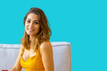 Jovem corretor de imóveis sorrindo e mostrando chaves com casa ao fundo