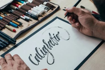 Pessoa praticando caligrafia com caneta e caderno, foco nos detalhes da escrita elegante.