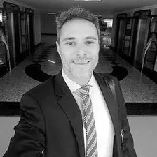 Homem de negócios confiante negociando em uma reunião, com gráficos de vendas em alta ao fundo, representando o curso Conquer.